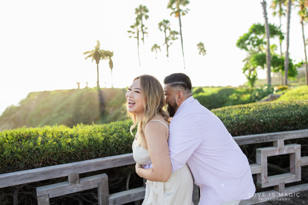 couple laughs in glowy sunlight with palm trees in the background, photo by Love is Magic Photography