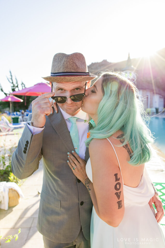Sunglasses on groom as bride kisses him in front of resort pool