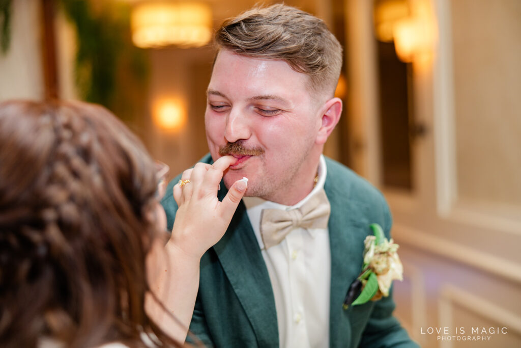 groom licks cake off brides finger, photo by Love is Magic Photography