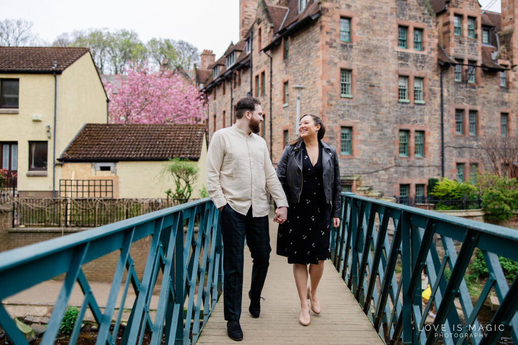 Edinburgh engaged couple hold hands on a bridge in Dean Village