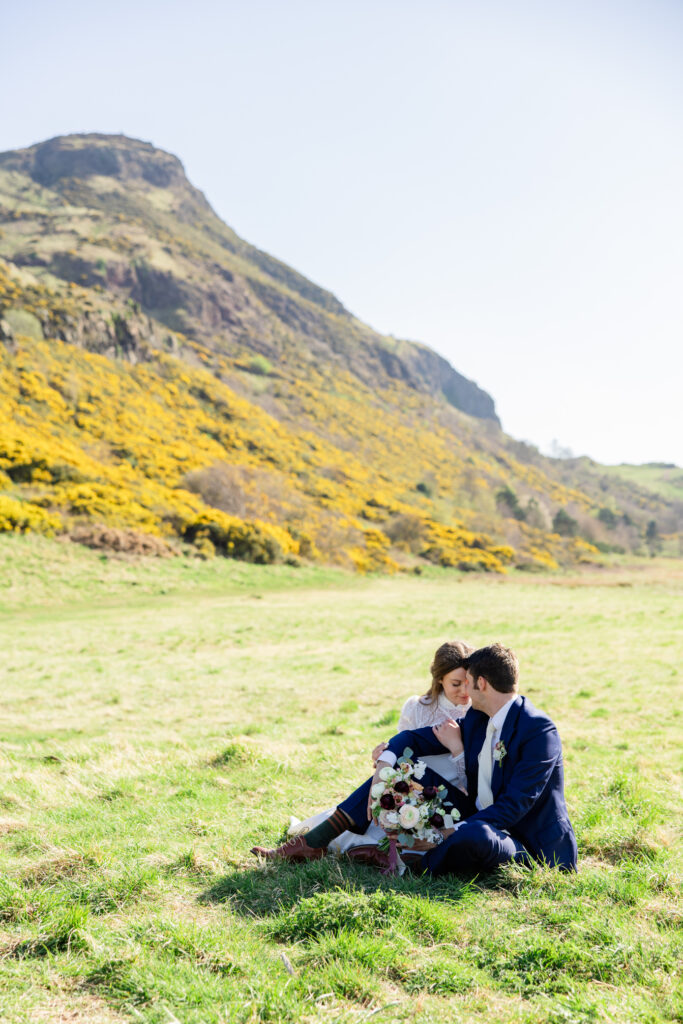 couple sitting in a field under Arthur's Seat couple sitting in a field under Arthur's Seat