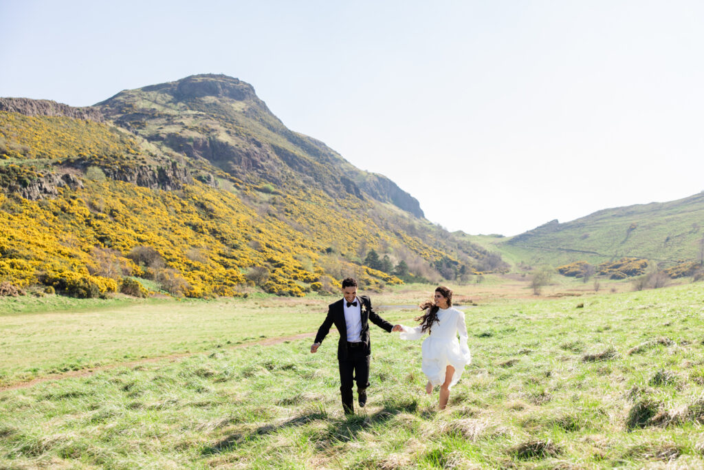 bride and groom hold hands and running on Arthur's Seat bride and groom hold hands and running on Arthur's Seat