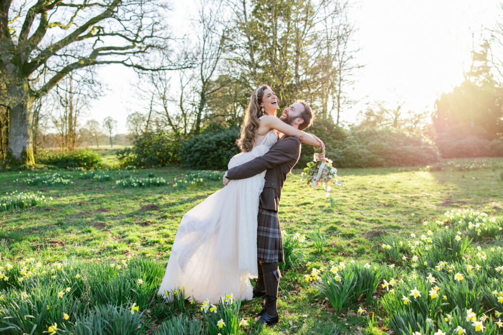 kilt wearing groom lifts bride in glowy sun