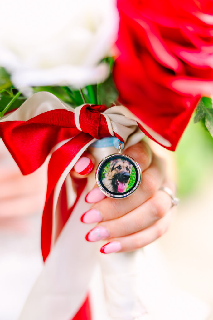 Bridal bouquet with red and white roses featuring a memorial photo charm of a beloved dog