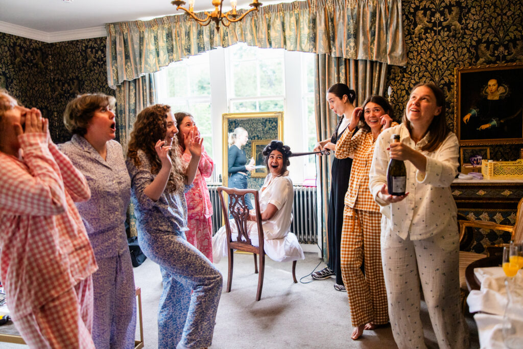 Bride and bridesmaids reacting to popping champagne with excitement while getting ready at Melville Castle wedding venue