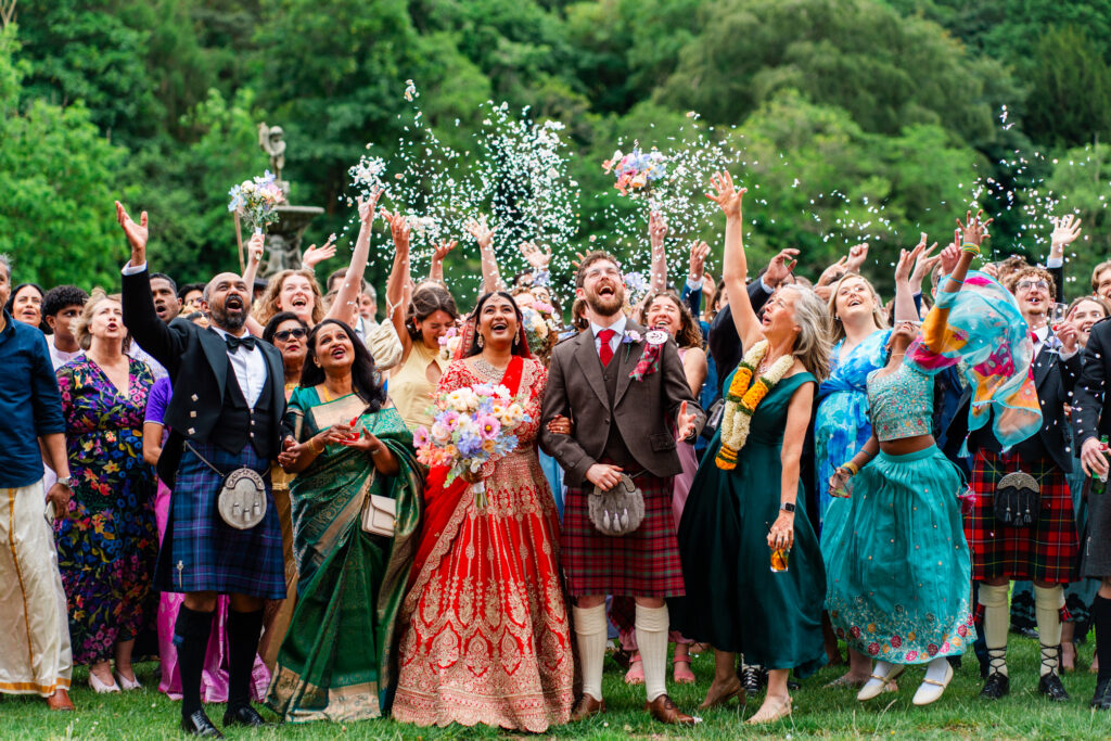 Bride and groom celebrate with family and friends during a joyful confetti moment in the gardens at Melville Castle