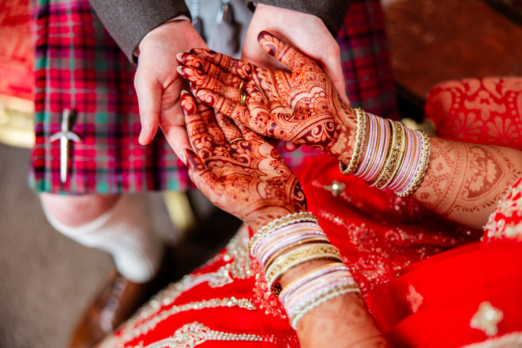 Bride and groom holding hands, highlighting intricate mehndi and wedding rings