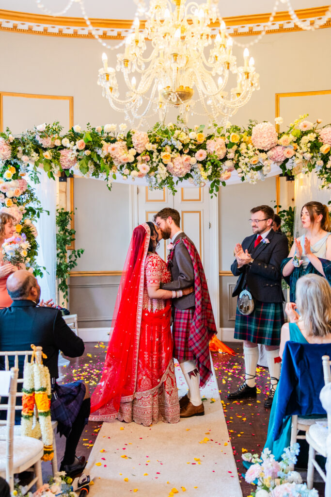 Bride and groom share their first kiss beneath a pastel floral arch during their Melville Castle wedding ceremony