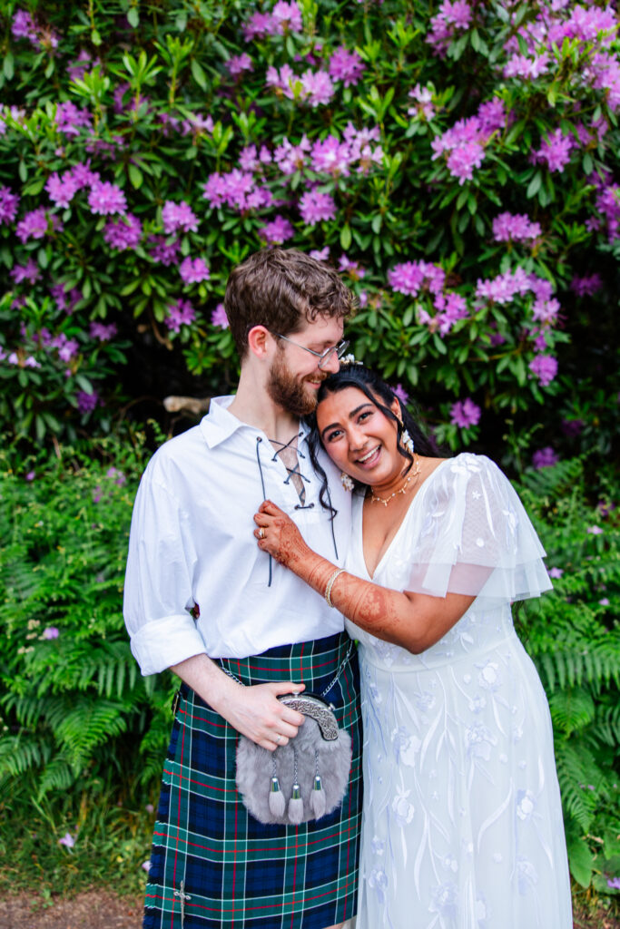 Bride embracing her groom in a Scottish kilt in front of blooming purple rhododendrons during portraits at Melville Castle wedding venue