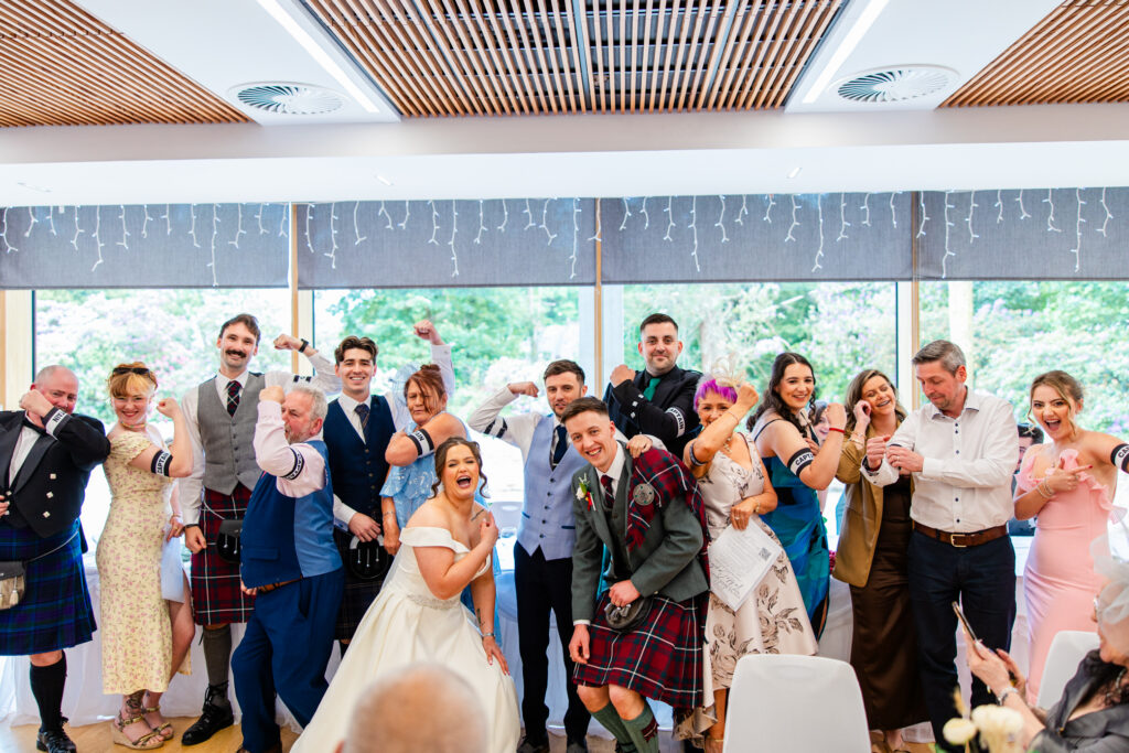 Bride, groom and wedding guests posing together during a fun reception game at Kilmardinny House