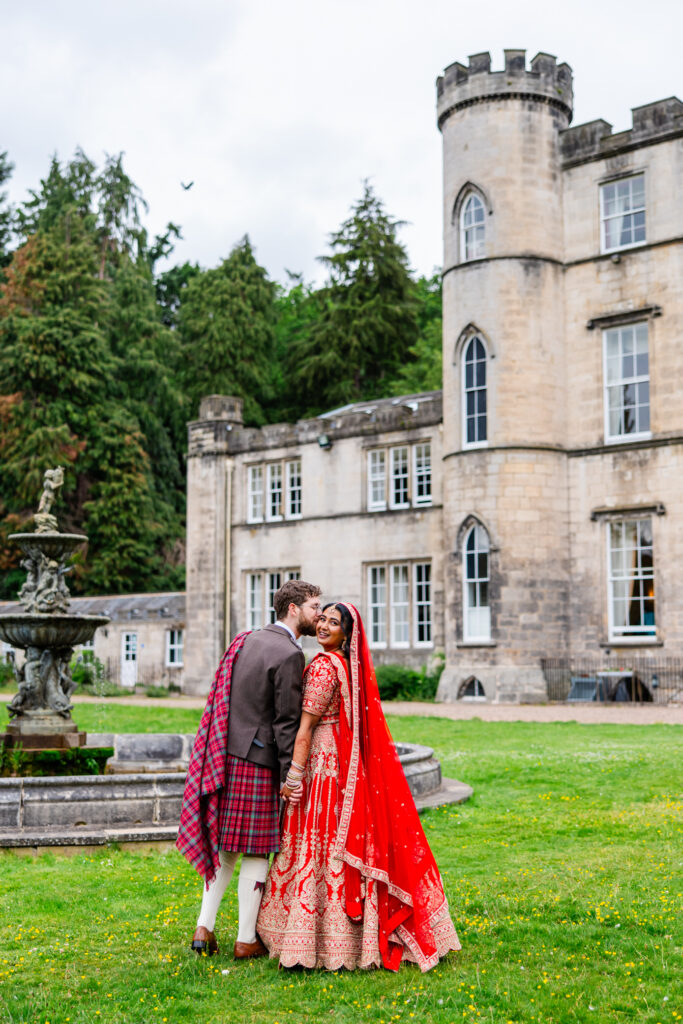 Bride in a red bridal lehenga and groom in a Scottish kilt outside Melville Castle during their wedding portraits