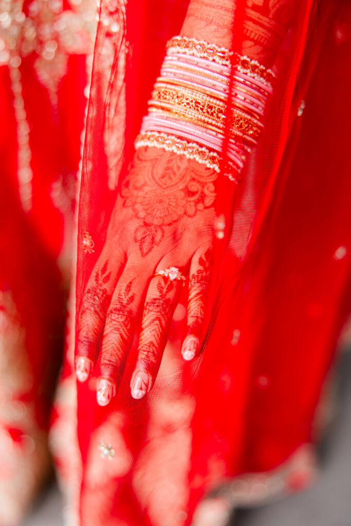 Close-up of the bride's engagement ring, bangles and henna beneath a red bridal veil