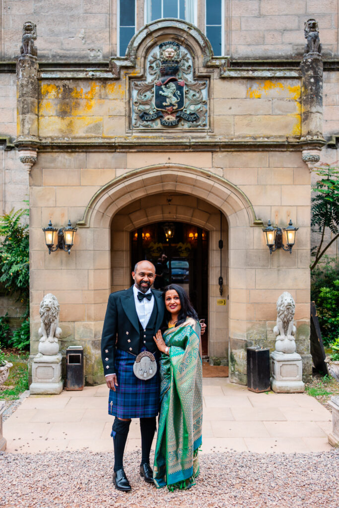 Couple wearing traditional Scottish and Indian wedding attire outside the entrance to Melville Castle