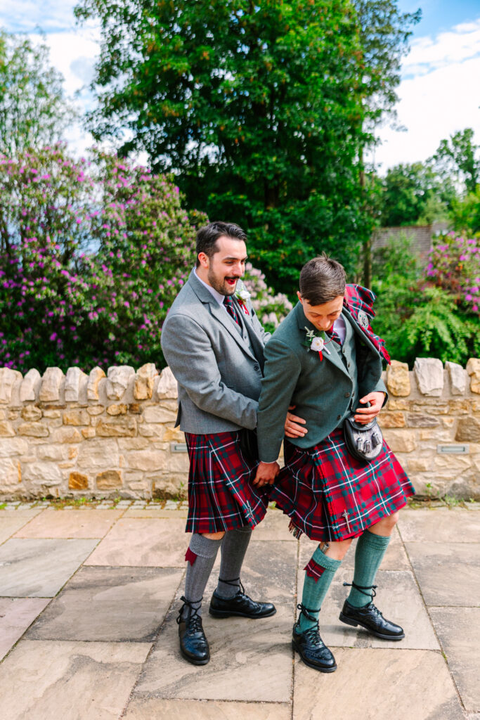 Groom and groomsman laughing together during relaxed wedding portraits at Kilmardinny House