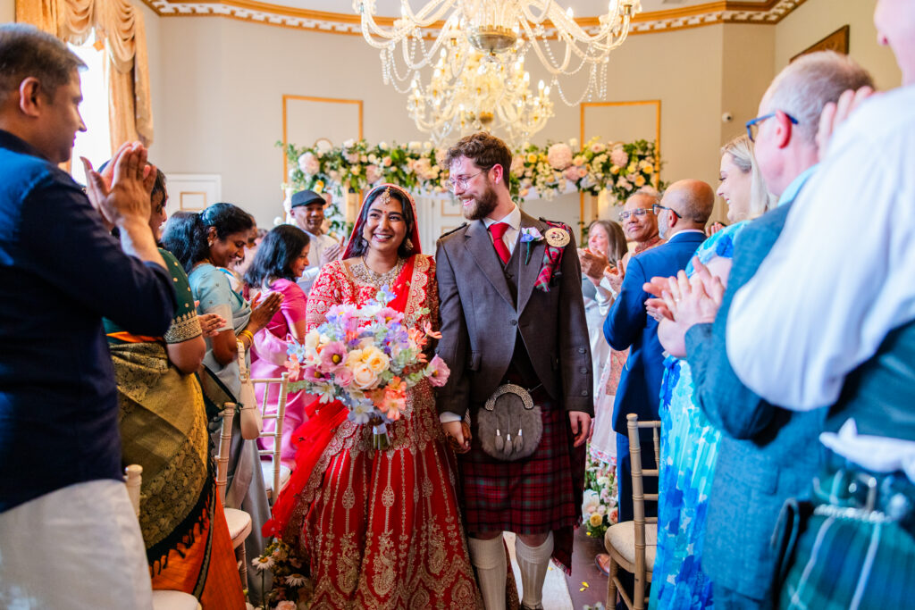 Newly married couple walk down the aisle smiling as guests applaud after their Melville Castle wedding ceremony