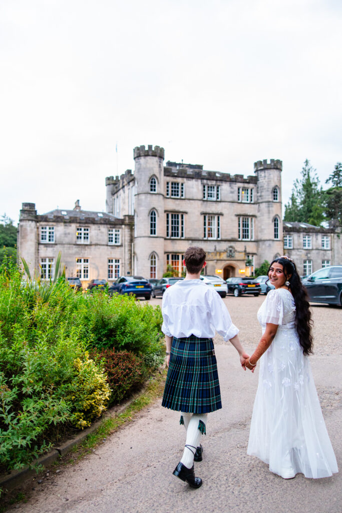Newlyweds holding hands in front of the historic Melville Castle surrounded by gardens after their Edinburgh wedding ceremony
