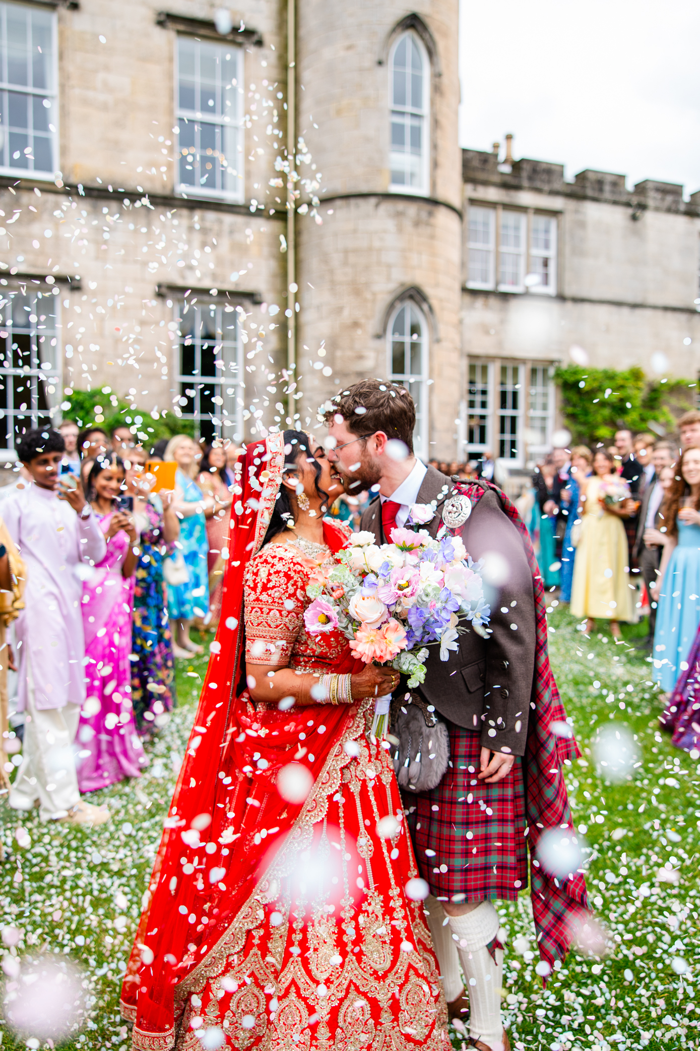 Romantic confetti kiss outside Melville Castle with guests celebrating a colourful Scottish and Indian wedding