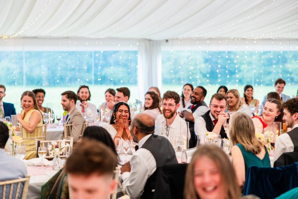 Wedding guests laughing during speeches inside the fairy-lit marquee at Melville Castle