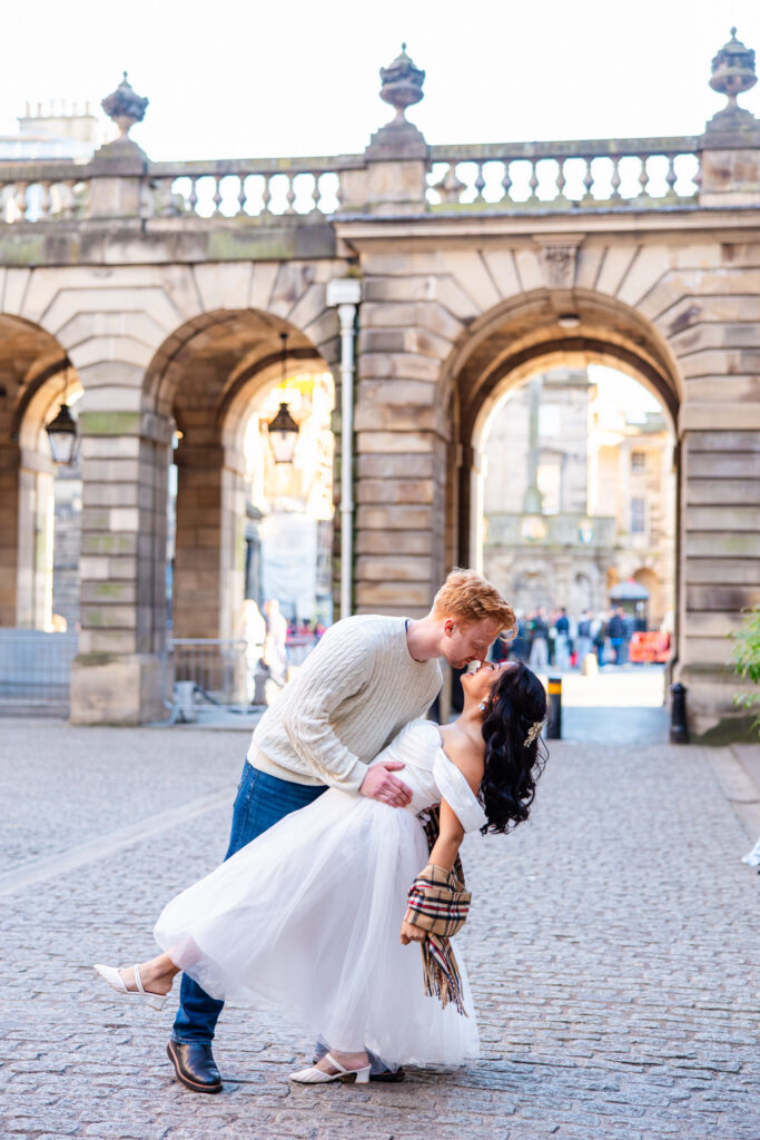 Bride and groom sharing a playful dip on a historic Edinburgh street during their wedding portraits