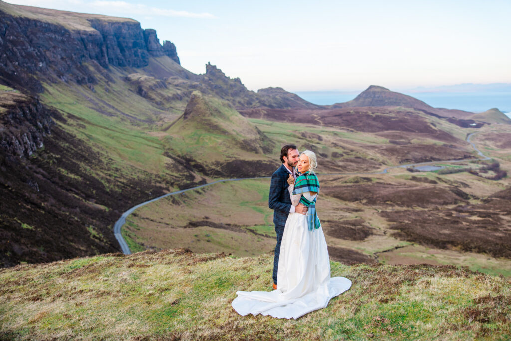Bride in a white wedding dress standing with her partner in the dramatic Quiraing landscape