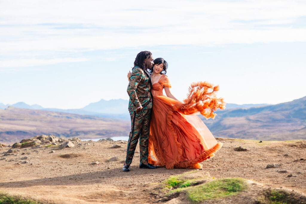 Couple embracing as a flowing orange wedding dress catches the wind on the Isle of Skye