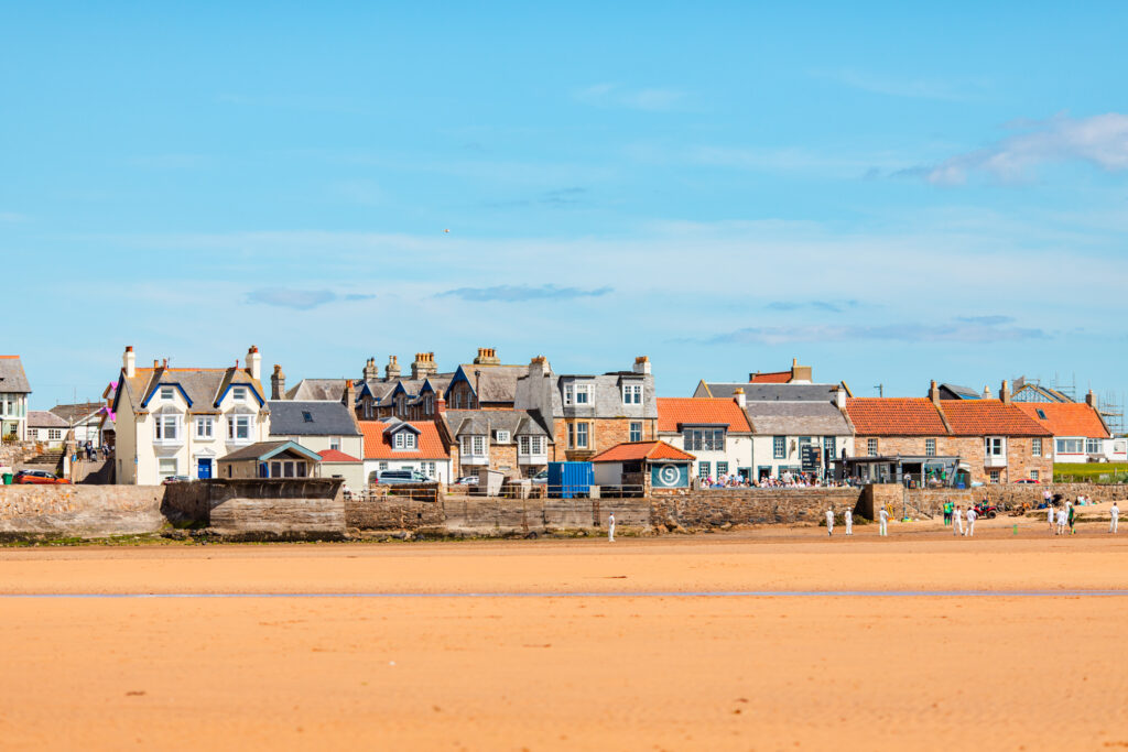 Elie beach in Fife with colourful seaside restaurant overlooking the cricket match on the sandy shore