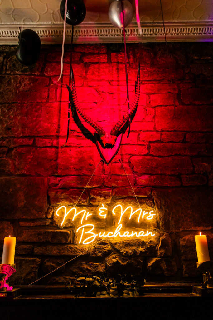 Neon wedding sign reading Mr and Mrs Buchanan above candles at the reception