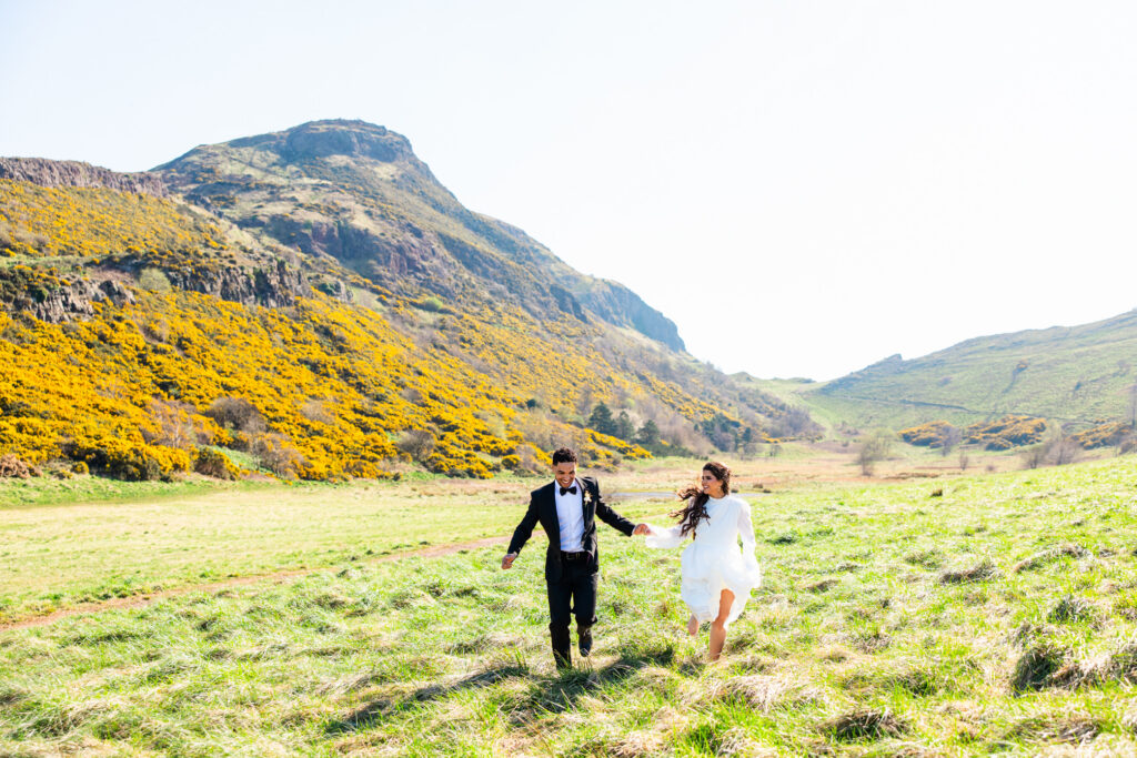 Newlywed couple running together in the sunshine during their Arthur’s Seat elopement