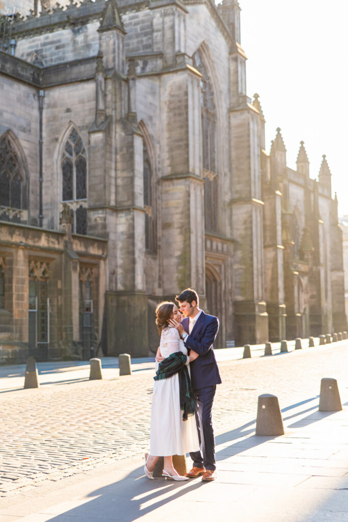 Newlywed couple embracing beside a historic Edinburgh church during their wedding portraits