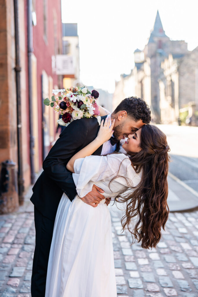 Newlywed couple sharing a kiss on Edinburgh's Royal Mile with historic buildings behind them