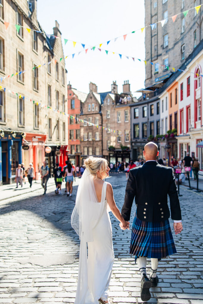 Newlyweds walking through colourful Victoria Street in Edinburgh Old Town