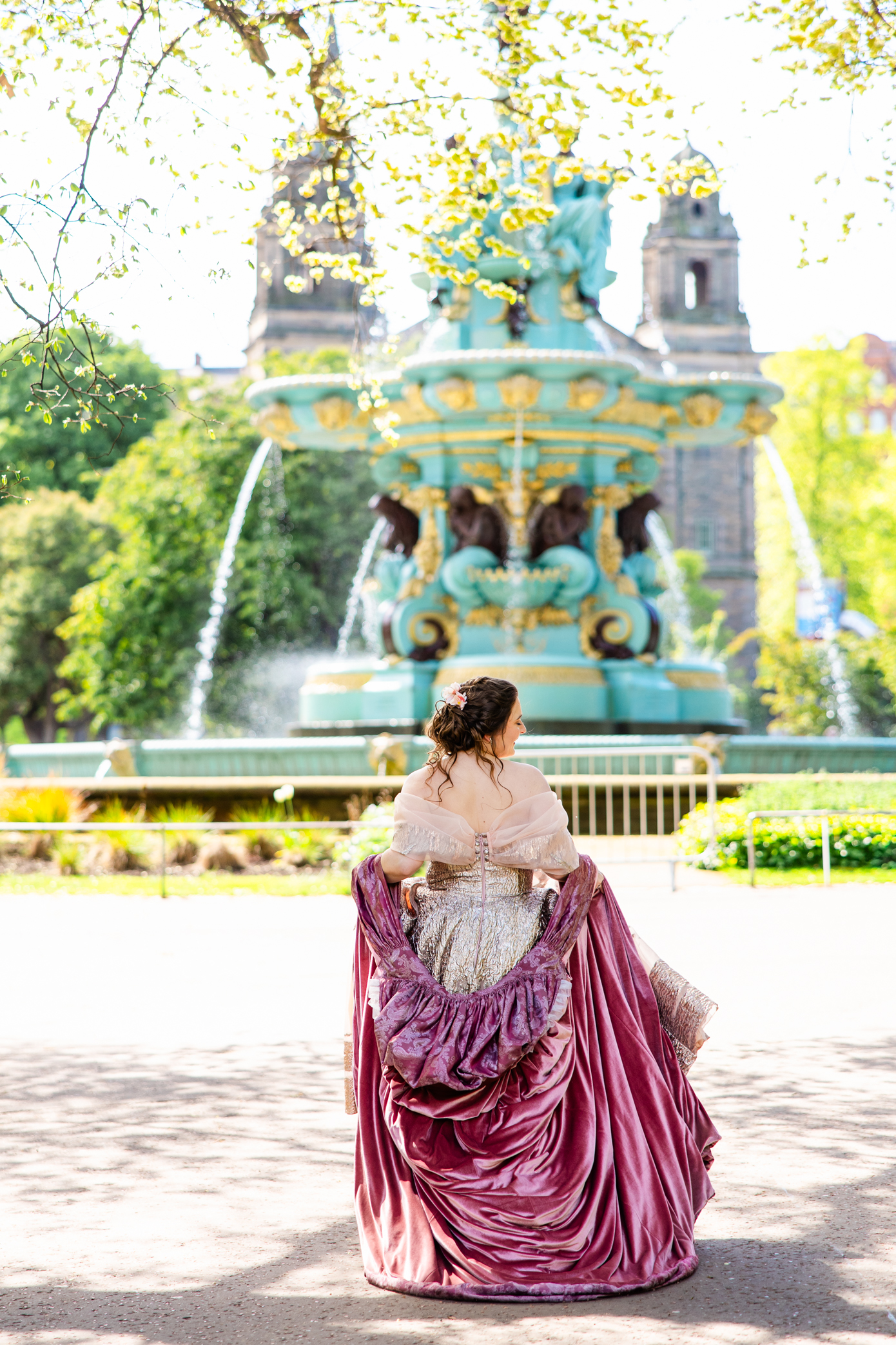 Woman in a medieval ball gown standing in front of Ross Fountain in Princes Street Gardens, Edinburgh